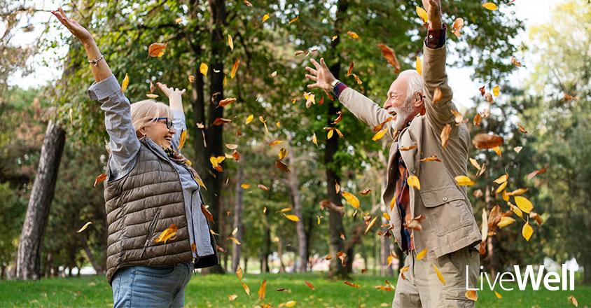 elderly man and woman laughing outside amongst fall leaves